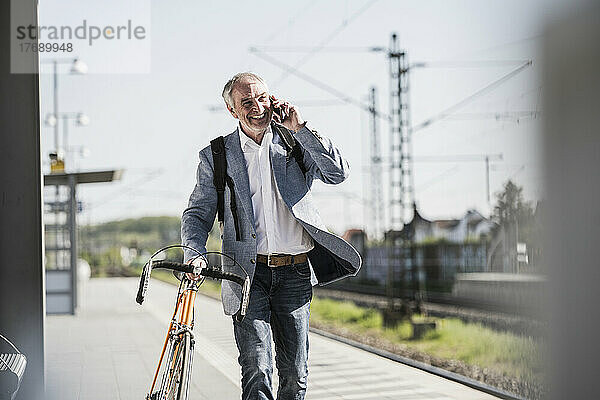 Glücklicher Geschäftsmann  der mit dem Handy telefoniert und am Bahnsteig mit dem Fahrrad unterwegs ist