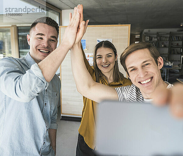 Fröhliche Geschäftsleute feiern High-Five und machen ein Selfie im Büro