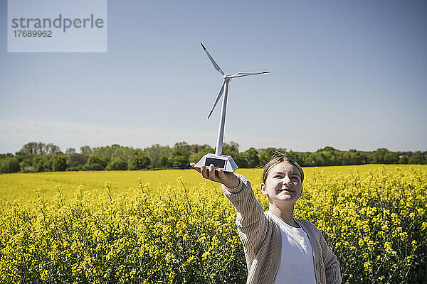 Glückliches Mädchen mit Modell einer Windkraftanlage  das an einem sonnigen Tag auf dem Feld steht