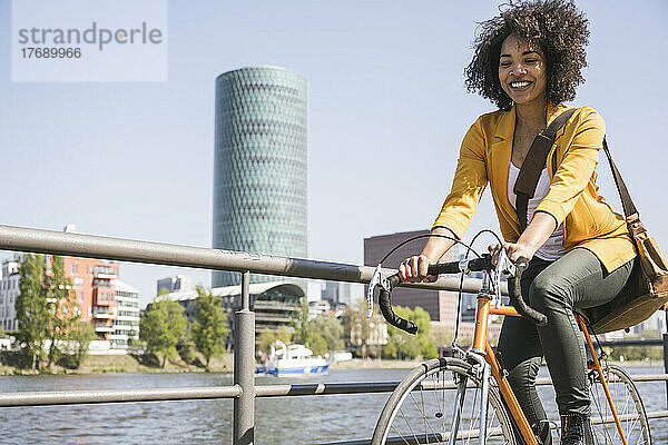 Glückliche Geschäftsfrau  die an einem sonnigen Tag mit dem Fahrrad am Main entlang fährt