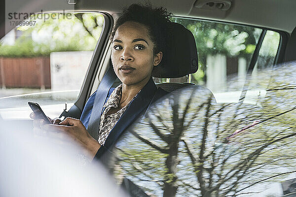 Nachdenkliche Geschäftsfrau mit Smartphone im Auto
