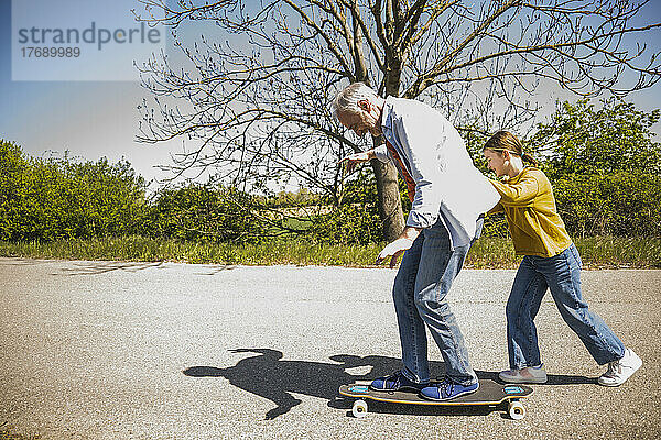 Verspieltes Mädchen drückt Großvater auf Skateboard