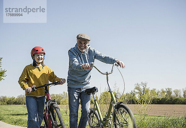Glücklicher Großvater und Enkelin  die an einem sonnigen Tag mit dem Fahrrad spazieren gehen