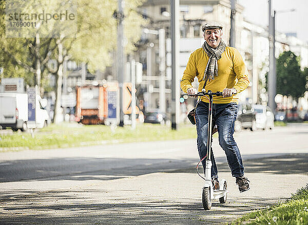 Glücklicher älterer Mann fährt mit Elektroroller auf dem Bürgersteig in der Stadt