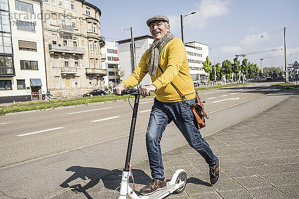 Glücklicher älterer Mann mit Elektroroller in der Stadt