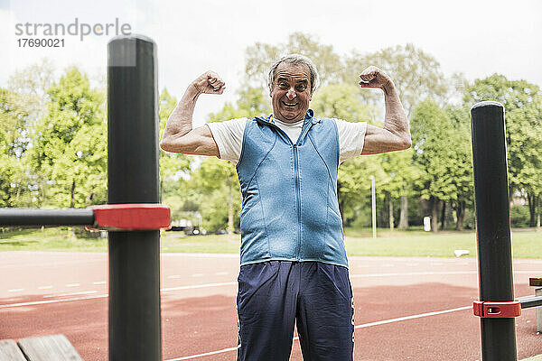 Glücklicher älterer Mann  der im Park Muskeln spielen lässt