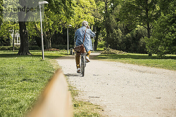 Älterer Mann fährt Fahrrad auf Fußweg im Park