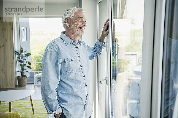 Happy senior man looking through window at home