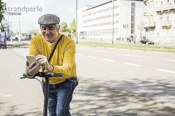 Lächelnder älterer Mann  der sein Mobiltelefon benutzt und sich auf einen Elektroroller stützt