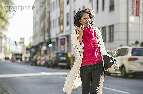 Glückliche Geschäftsfrau  die mit ihrem Mobiltelefon auf der Straße in der Stadt spaziert