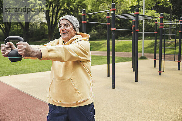 Glücklicher älterer Mann  der im Park mit der Kettlebell trainiert