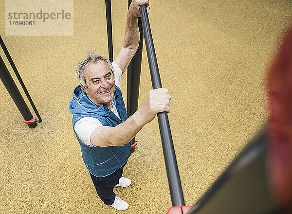 Lächelnder älterer Mann hält Gymnastikstange im Park