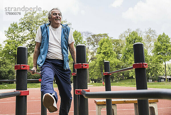 Glücklicher aktiver älterer Mann  der an der Gymnastikstange im Park trainiert