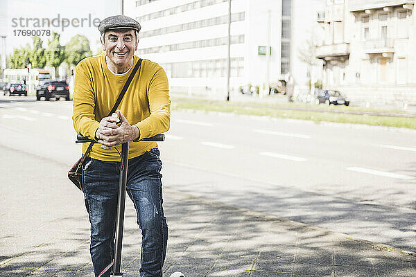 Glücklicher älterer Mann mit gefalteten Händen  der sich auf einen Elektroroller stützt