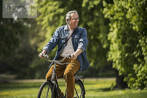 Glücklicher Mann mit Brille  der an einem sonnigen Tag im Park Fahrrad fährt