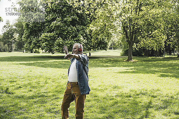 Glücklicher älterer Mann mit kabellosen Kopfhörern  der im Park Musik genießt