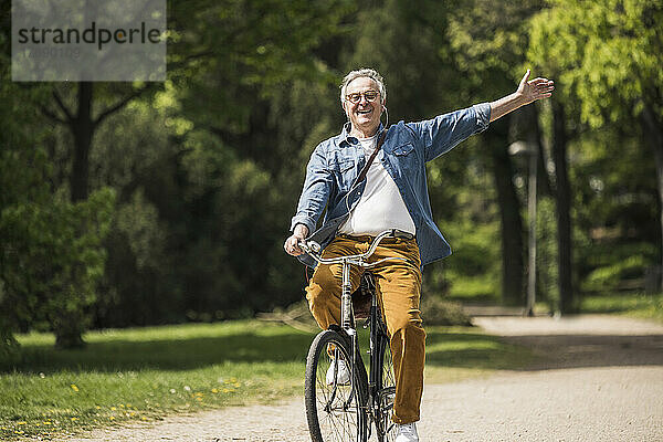 Glücklicher älterer Mann mit erhobenen Armen  der eine Radtour im Park genießt