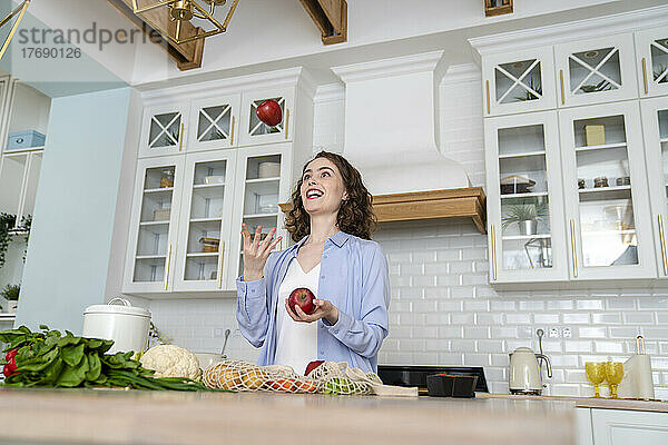 Glückliche Frau jongliert mit Äpfeln in der heimischen Küche