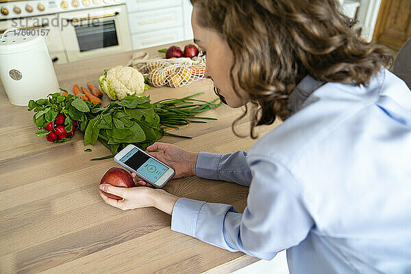 Junge Frau überprüft zu Hause die Kalorien des Apfels über die mobile App