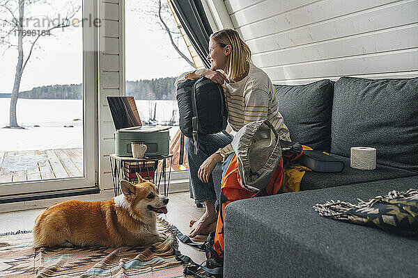 Frau mit Rucksack sitzt zu Hause neben Hund auf Sofa