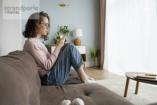 Junge Frau sitzt auf Sofa im Wohnzimmer
