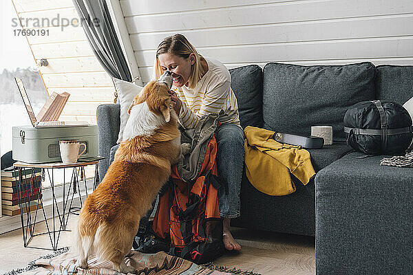 Lächelnde Frau streichelt Hund  der zu Hause auf dem Sofa sitzt