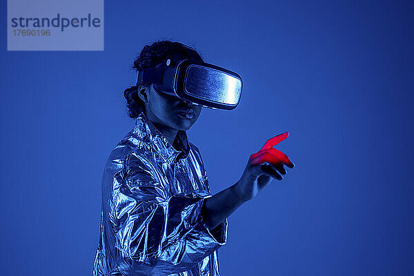 Junge Frau mit Virtual-Reality-Simulator gestikuliert vor blauem Hintergrund