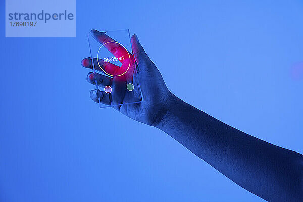 Hand einer Frau mit Stoppuhr auf futuristischem  transparentem Smartphone vor blauem Hintergrund