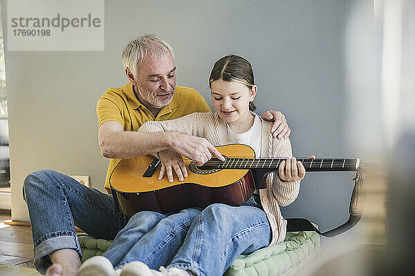 Glücklicher älterer Mann  der seiner Enkelin zu Hause Gitarre beibringt
