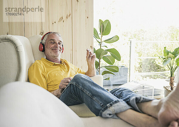 Glücklicher älterer Mann mit kabellosen Kopfhörern  der zu Hause auf dem Sofa sitzt