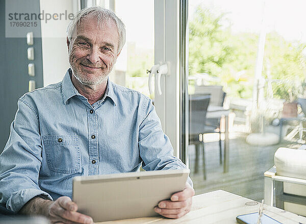 Happy senior man with tablet PC sitting at table