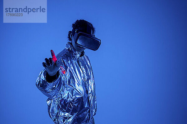 Frau mit Virtual-Reality-Simulator gestikuliert vor blauem Hintergrund