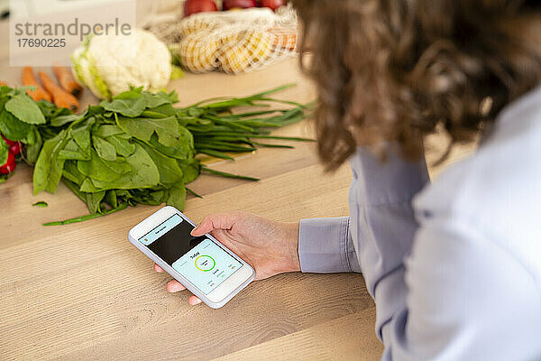 Frau nutzt mobile App beim Gemüse am Esstisch