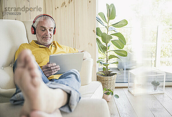 Älterer Mann trägt kabellose Kopfhörer und nutzt zu Hause ein digitales Tablet
