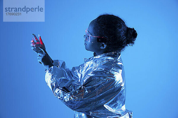 Junge Frau benutzt futuristisches Smartphone vor blauem Hintergrund