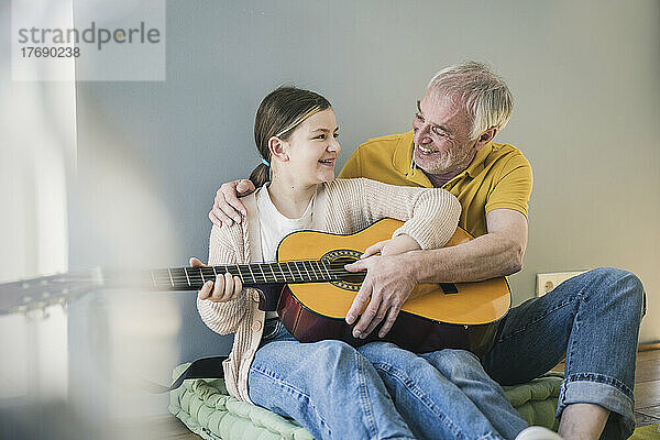 Glückliches Mädchen mit Großvater  der zu Hause Gitarre lernt