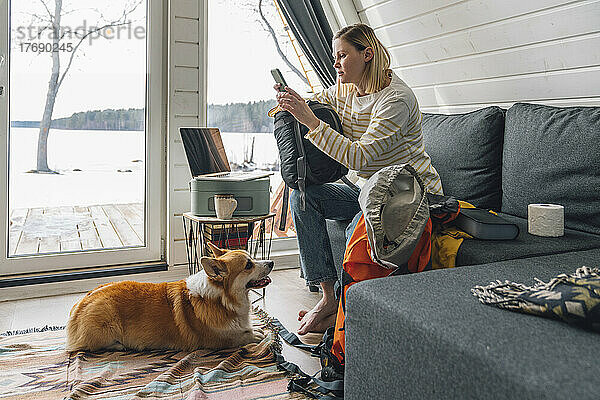 Frau benutzt Smartphone und sitzt zu Hause neben dem Rucksack auf dem Sofa