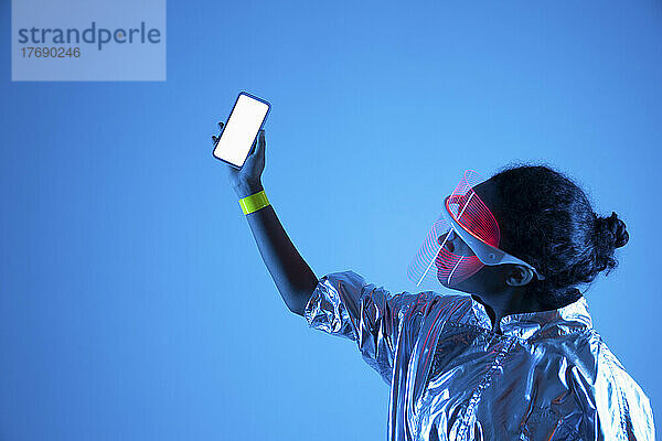 Frau mit Smart-Brille hält Smartphone vor blauem Hintergrund