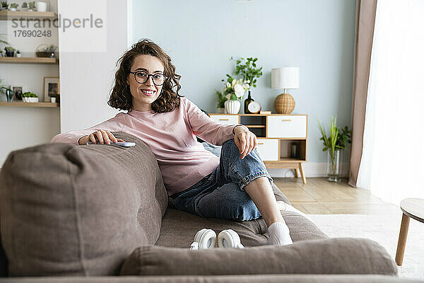 Lächelnde Frau sitzt zu Hause auf dem Sofa