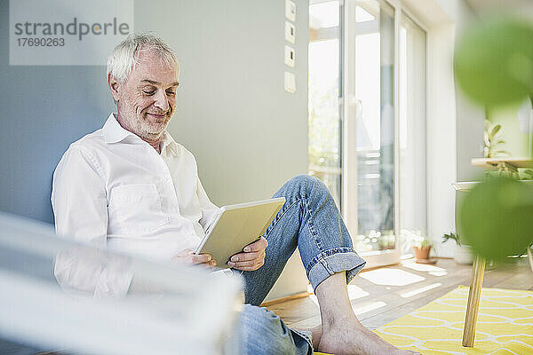 Lächelnder älterer Mann  der zu Hause einen Tablet-PC benutzt