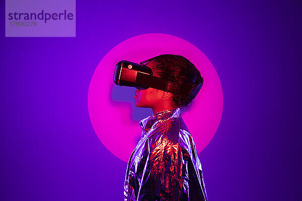 Im Rampenlicht steht eine junge Frau mit Virtual-Reality-Simulator vor violettem Hintergrund