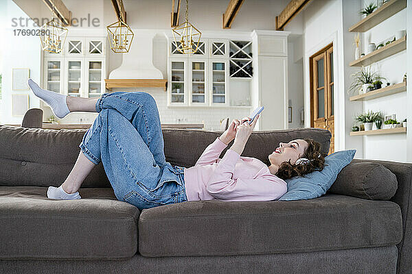 Frau benutzt Smartphone auf Sofa liegend