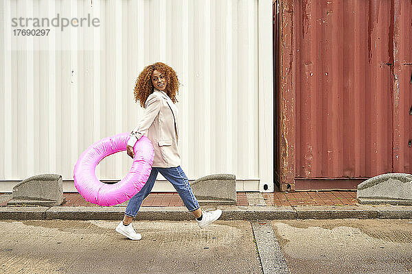 Verspielte Geschäftsfrau läuft mit rosa aufblasbarem Ring auf Fußweg