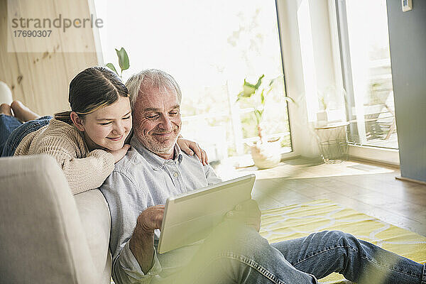 Lächelnder älterer Mann mit Enkelin  der zu Hause einen Tablet-PC nutzt