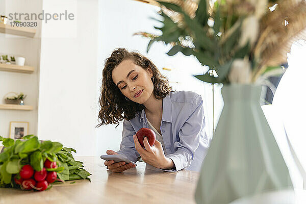 Junge Frau überprüft die Kalorien von Äpfeln auf dem Handy in der Küche