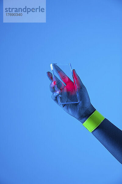 Hand einer Frau  die ein futuristisches  transparentes Smartphone vor blauem Hintergrund hält