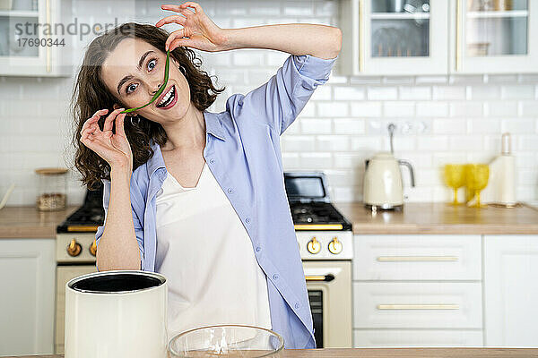 Fröhliche Frau macht zu Hause in der Küche Schnurrbart mit Frühlingszwiebelblatt