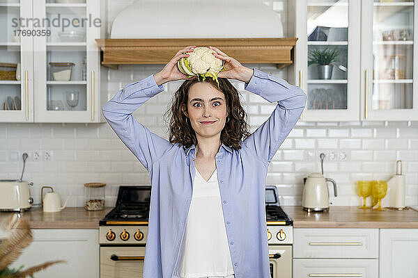 Junge Frau hält Blumenkohl auf dem Kopf in der heimischen Küche