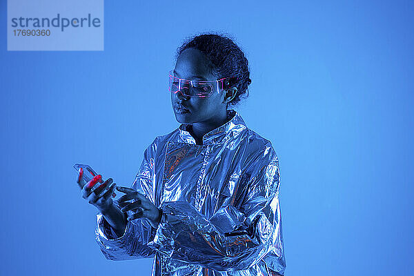 Junge Frau benutzt futuristisches transparentes Smartphone vor blauem Hintergrund