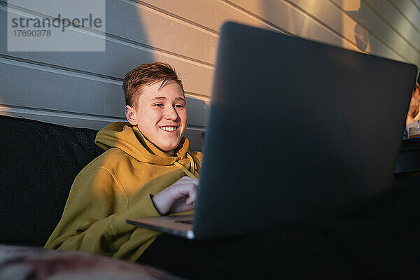 Lächelnder Junge  der zu Hause einen Laptop benutzt